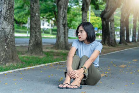 Portrait of young Asian woman enjoying and relaxing outdoors. Cheerful teenage female sitting on the road in the park on a sunny summer day. Summer active lifestyle concept and copy space for text.の写真素材
