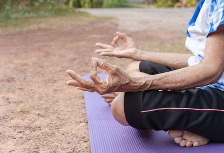 Closeup of aged woman hands meditating in lotus position on yoga mat at rural. Calm senior female practice yoga outdoors at home relieving stress, peaceful lady follow healthy lifestyle do exerciseの写真素材