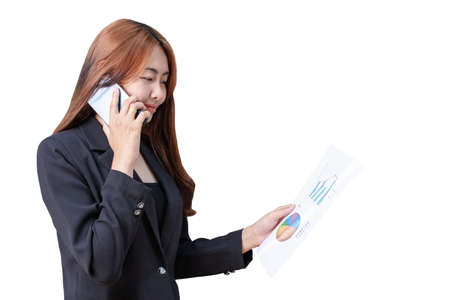 Portrait of young Asian businesswoman talking with colleague on smartphone. Smiling successful female reading paper document with graphs and financial reports. Copy space for text and white backgroundの写真素材