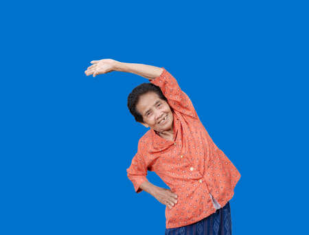 Portrait Of active senior old woman warming stretching exercising isolated on blue background. Happy...