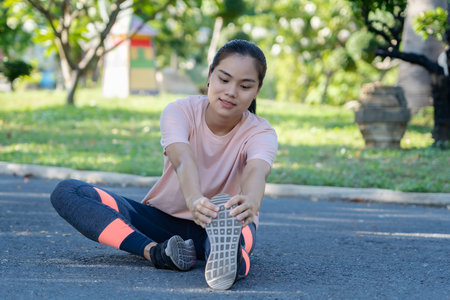 Happy young fitness woman doing stretch exercise outdoors in park. Asian female stretching her arms and legs for warming up before running or working out in morning. Healthy and Lifestyle Concept.の写真素材