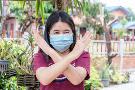 Adult woman wearing medical face mask. Pretty middle female holding two arms crossed, showing stop...