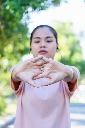 Close up hands of young woman stretching before exercise at the park. Happy Asian female enjoying workout outdoor with sunlight. Selective focus on hands with blurred face lady. Good Health, Wellness.の写真素材