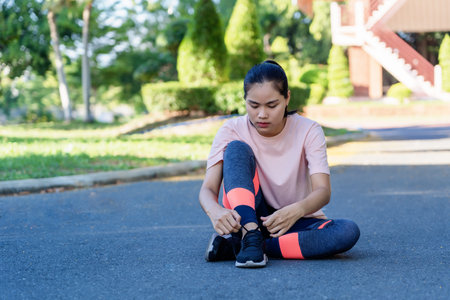 Portrait of healthy young woman tying running shoes and sitting on street before running. Female...