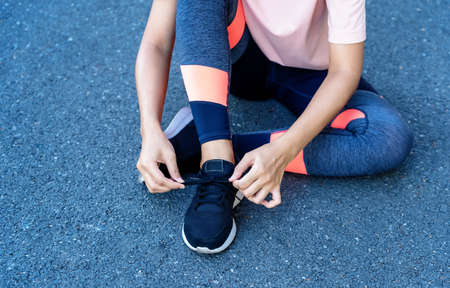 Close up of hands touching running shoes and legs woman sitting on the street. Female athlete jogging and training outdoors. Healthy and Lifestyle conceptの写真素材