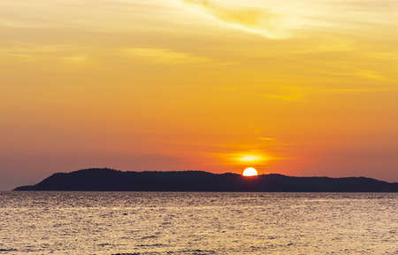 Landscape of colorful sunset shining over bright orange waters of the ocean. Silhouette of tourists walking, relaxing and taking photos sundown on beach of tropical sunset at Koh Larn Beach.の写真素材