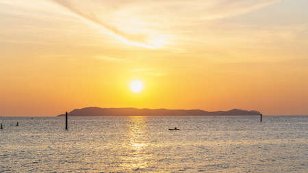 Landscape of colorful sunset shining over bright orange waters of the ocean. Silhouette of tourists walking, relaxing and taking photos sundown on beach of tropical sunset at Koh Larn Beach.の写真素材