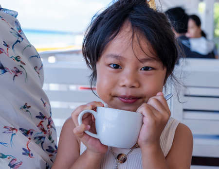 Portrait of a sad little girl sitting on chair on balcony looking at sand on beach at restaurant beside beach in the morning sunrise. In sad mood.の写真素材