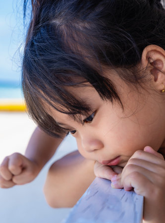 Portrait of a sad little girl sitting on chair on balcony looking at sand on beach at restaurant...
