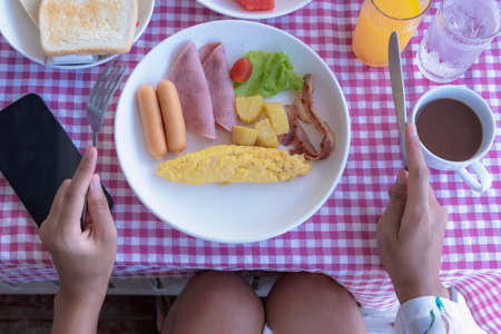 Fresh breakfast table with omelet roll, sausage, bacon, ham, tomato and potato on a dish. Woman's...