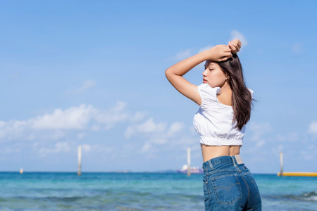 Lifestyle image of carefree traveling woman standing on sandy beach near turquoise colored ocean in summertime. Female tourist with straw hat in hands enjoying traveling to exotic nature leisure time.の写真素材