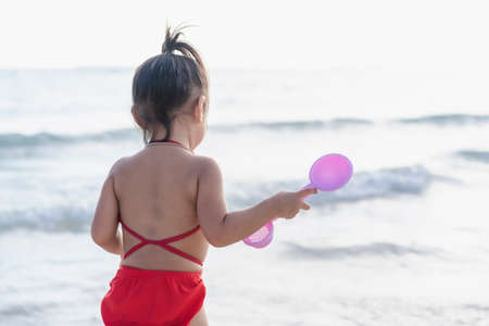 Adorable little girl in swimsuit at tropical beach. Preschool girl having fun with playing with sand on lake on summer day outdoors. Happy child learning swimming. Active leisure with kid on vacationsの写真素材