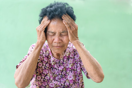 Senior black-haired woman touching head with hand with painful expression because of headache. Mature woman suffering from headache at home. Health care conceptの写真素材