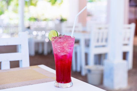 Cold red Juice with iced cub and a slice of lemon on top of glass on table at restaurant. Glass of...