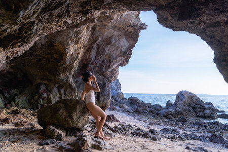 Portrait of beautiful fashionable woman in white bikini posing at the rock beach. Young Asian woman dressed in swimsuit standing on a rock on summer day with sunset backgrounds at Koh Larn in Pattayaの写真素材