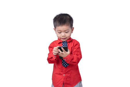 Little small smiling happy boy 3-4 years old wearing a red shirt and holding in hand play smartphone isolated on white background studio portrait. Children and gaming addiction and lifestyle conceptの写真素材