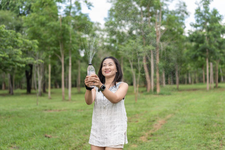Happy young woman holding a water bottle in her hand Her cheerful demeanor and relaxed demeanor reflect the happiness she finds in her peaceful surroundings. during the summer Lifestyle of happiness.の写真素材