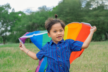 Happy little child holds a rainbow flag, a symbol of inclusivity regarding gender identity. It represents diversity and acceptance. The flag flutters in the wind. Supporting the LGの写真素材