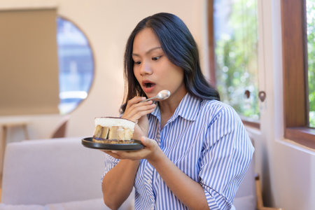 Happy woman opens mouth wow, staring at cake in hand, spoon in hand enjoying her favorite dessert.の写真素材