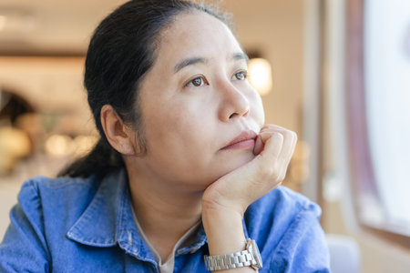 A tired and unhappy young woman sits with her chin raised on a sofa at a cafe. Looking outside, feeling stressed and irritated Bored and fed up with negative ideas.の写真素材