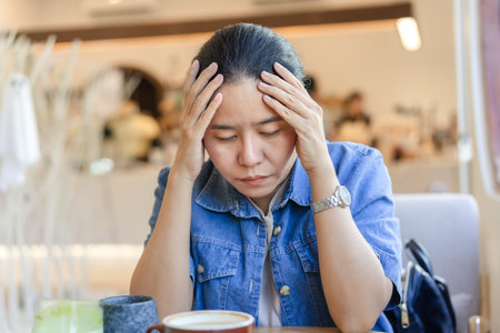 Asian woman who feels sick or has a headache. Puts her hands on her temples and closes her eyes. Expression and posture. stress worry, and Problems that plague migraines.の写真素材