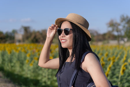 Female had a beautiful smile, wore a straw hat, and wore sunglasses. Enjoy happy and relaxed nature, and warm sunshine, during outdoor time on a hot summer day. sunflower field background.の写真素材