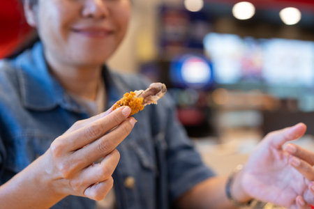 Close-up of a happy smiling young woman's hand holding a bite of fried chicken in her hand. Delicious fried chicken in a shop selling chicken drumsticks.の写真素材