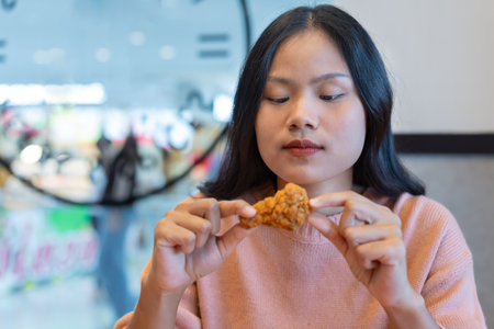 Asian woman looked at the fried chicken in her hand and hesitated. to eat delicious fried chicken in hand Concepts about unhealthy food, high fat food, obesity, trans fat, saturated fat. Food concept.の写真素材