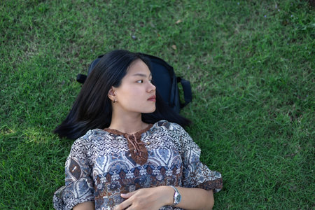A beautiful young woman is resting, lying on the grass in the park. Relax during your summer holidays on the comfortable lawns. A time of solitude.の写真素材