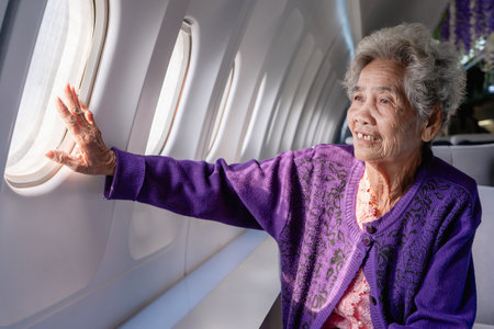 Senior gray haired woman looking out the airplane window. Portrait of an elderly woman sitting in a...