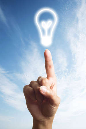 light bulb glowing on finger over blue skyの写真素材