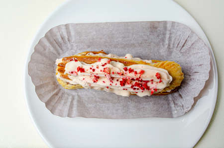 Eclair with cream and strawberries. On a white plate High quality photo