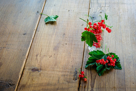 Red currants in a glass. On a wooden background, a light green napkin with leaves and red berries, on a napkin a glass transparent glass with red currant berries. High quality photoの写真素材
