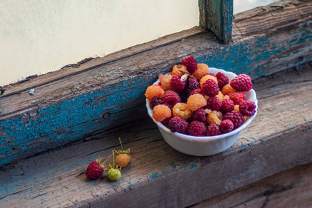 Raspberries in a white cup. On a wooden background with green leaves. A vase of red and white raspberries on boards. High quality photoの写真素材