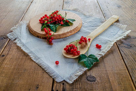 Red currants in a glass. On a wooden background, a light green napkin with leaves and red berries, on a napkin a glass transparent glass with red currant berries. High quality photoの写真素材