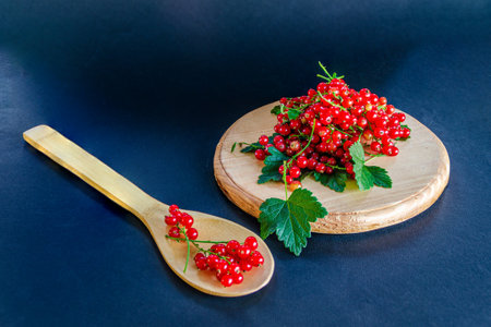 Red currants in a glass. On a wooden background, a light green napkin with leaves and red berries,...