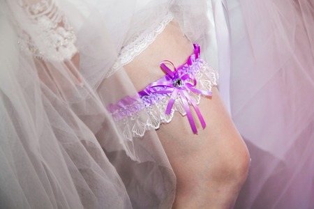 Bride's garter, wedding garter on leg of bride. Clothes of bride and white lingerie. White dress and stockings. Dressing the bride of sexy touch.の写真素材