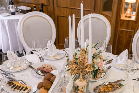 Elegant table setting with white tablecloth, candles, floral centerpiece and formal dining...