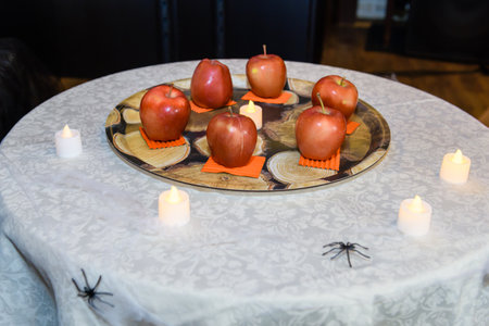 Candles on a table with red apples and spiders in the backgroundの写真素材
