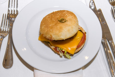 Hamburger with cheese and vegetables on a white plate in a restaurantの写真素材