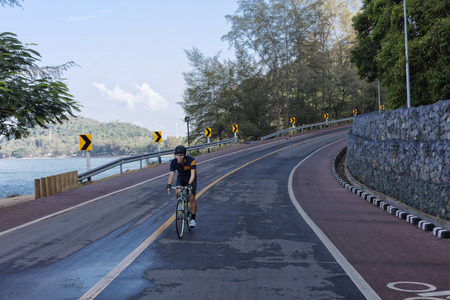 The asian racing biker cycling downhill on the seafront road.の写真素材