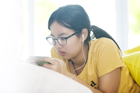 asian young girl lying on the bed and listening to music with smartphone in the bed roomの写真素材