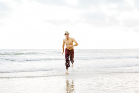 Young man running towards the camera from the seashore smiling.の写真素材