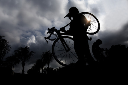 Silhouettes of man carrying  bike while walking at sunsetの写真素材