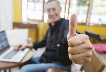 Casual smiling businessman showing thumbs up to camera in his officeの写真素材