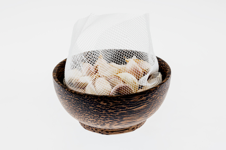 A meshed bag of garlics on the wooden bowlの写真素材