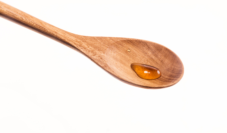 Tiny drops of honey in a wooden spoon over white backgroundの写真素材