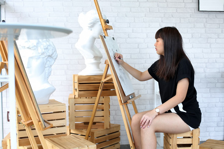 young woman  sketching on easel with pencil in brightly lit studio.の写真素材