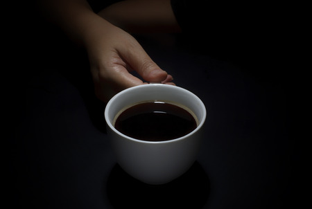 Hand holding a cup of coffee on black backgroundの写真素材