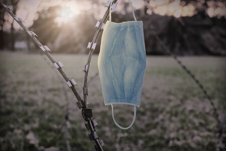 Medical mask hanging on barbed wire. Concept of quarantine or epidemic zone or pandemic prevention